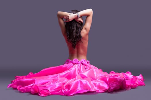 Studio portrait of dancer posing topless in pink costume sitting on floor