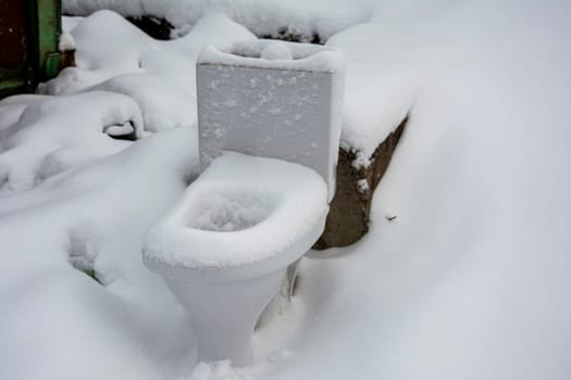 an old disassembled toilet bowl standing on the ground and covered with snow. landfill, repair