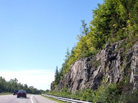 Rocks overgrown with green bushes and trees along the road to Ontario