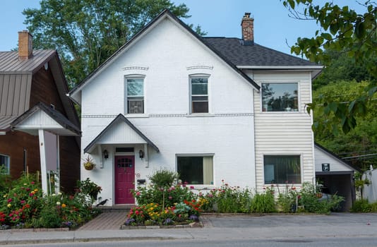 The facade of a small house is decorated with flower beds with colorful flowers.