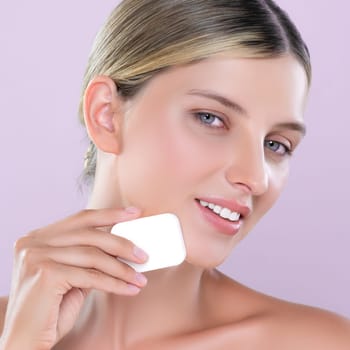 Closeup alluring beautiful female model applying powder puff for facial makeup concept. Portrait of flawless perfect cosmetic skin woman put powder foundation on her face in pink isolated background.