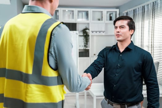 An engineer with a protective vest handshake with an investor in his office. Following a successful meeting, employee and employer form a partnership.