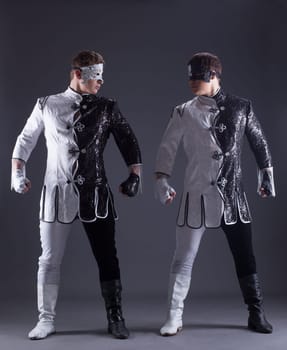 beautiful men posing in masquerade costumes, on gray background