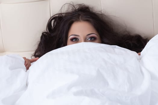 Portrait of young brunette covering bedsheet, close-up