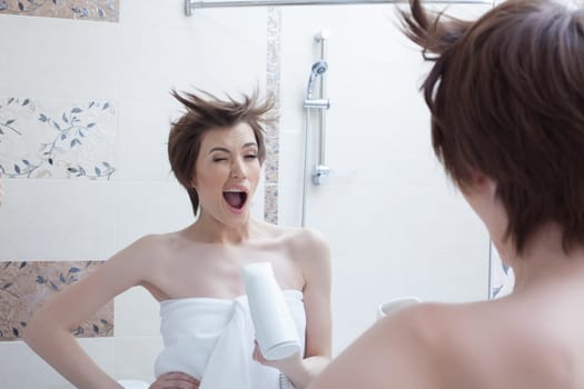 Cheerful girl posing with hairdryer near mirror in bathroom