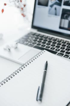 Close up view of notepad with pen on it and laptop at background.