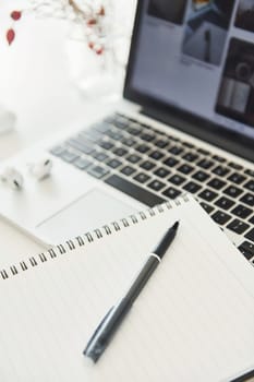 Close up view of notepad with pen on it and laptop at background.