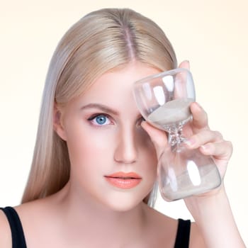 Personable model hold hourglass in aging young beauty concept of anti-aging skincare treatment for woman. Beautiful girl with smooth flawless natural facial skin in isolated background.