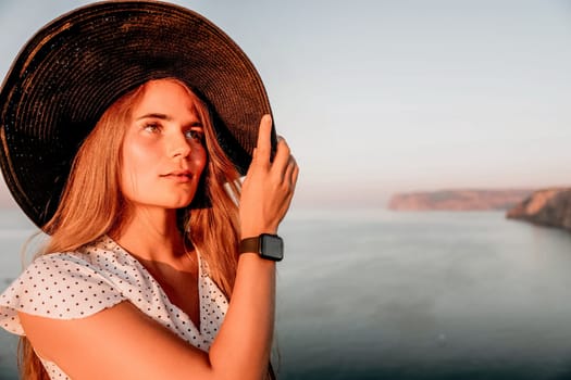 Portrait of happy young woman wearing summer black hat with large brim at beach on sunset. Closeup face of attractive girl with black straw hat. Happy young woman smiling and looking at camera at sea