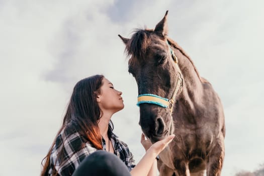 Cute happy young woman with horse. Rider female drives her horse in nature on evening sunset light background. Concept of outdoor riding, sports and recreation.