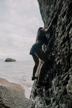 A girl climbs a rock. The athlete trains in nature. Woman overcomes difficult climbing route. Extreme hobby. Tourist woman rock climber hiking on mountains rocks over beautiful sea coast