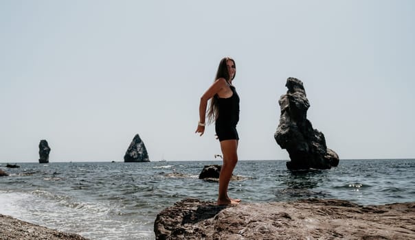 Woman travel sea. Young Happy woman in a long red dress posing on a beach near the sea on background of volcanic rocks, like in Iceland, sharing travel adventure journey