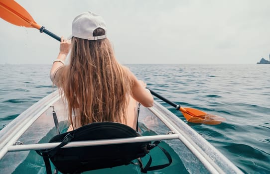 Woman in kayak back view. Happy young woman with long hair floating in transparent kayak on the crystal clear sea. Summer holiday vacation and cheerful female people having fun on the boat.