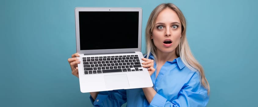 photo of shocked surprised cute blond girl with open laptop with blank space for website on blue background.