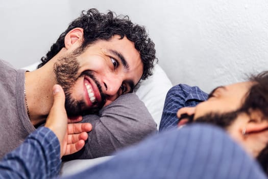 happy gay male couple relaxing in bed caressing face, concept of real people lifestyle at home and love between people of the same sex