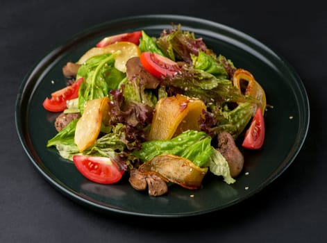lettuce salad with liver, caramelized pears and tomatoes on a dark