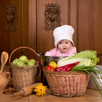 Portrait of a smiling baby sitting inside a large cooking stock pot surrounded by vegetables and food