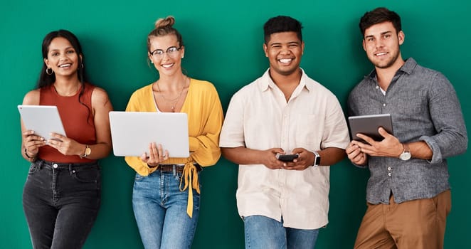We use social media to connect and engage with customers. Portrait of a group of young designers using digital devices while standing together against a green background