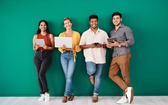 We cant function without our connections. Portrait of a group of young designers using digital devices while standing together against a green background