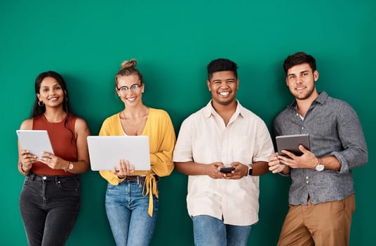 As business grows, so do our connections. Portrait of a group of young designers using digital devices while standing together against a green background