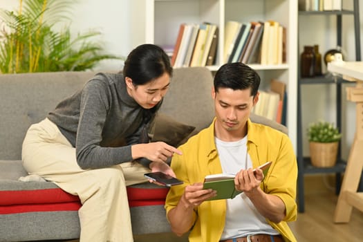 Happy young couple relaxing, reading book, enjoying leisure time on weekend at home.