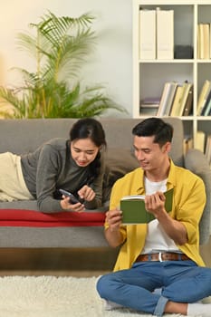 Happy married young couple reading book, enjoying leisure time on weekend at home.