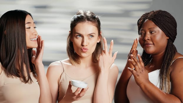 Interracial women applying moisturizing face cream, using skincare cosmetics to prevent wrinkles on camera. Beauty models advertising campaign for dermatology products. Skincare routine.