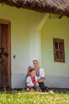 mother and daughter in traditional Ukrainian clothes are sitting near the house