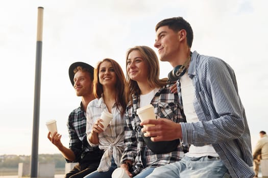 Sunny weather. Drinking coffee. Group of young cheerful friends that is outdoors having fun together.