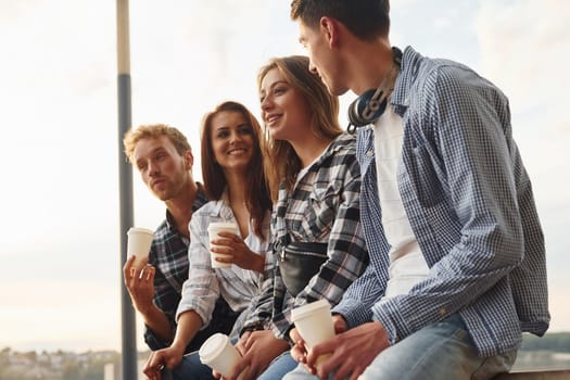 Sunny weather. Drinking coffee. Group of young cheerful friends that is outdoors having fun together.