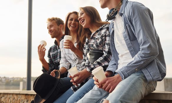 Sunny weather. Drinking coffee. Group of young cheerful friends that is outdoors having fun together.