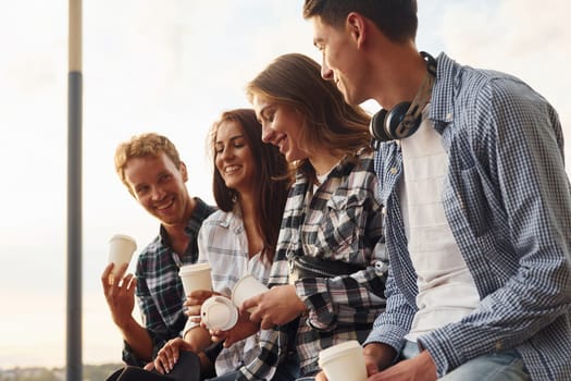 Sunny weather. Drinking coffee. Group of young cheerful friends that is outdoors having fun together.