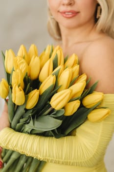 a happy woman in a yellow dress embraces a bouquet of yellow spring tulips in the interior.