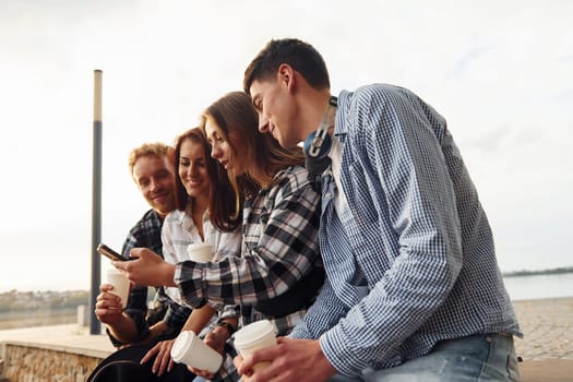 Sunny weather. Drinking coffee. Group of young cheerful friends that is outdoors having fun together.