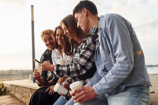 Sunny weather. Drinking coffee. Group of young cheerful friends that is outdoors having fun together.