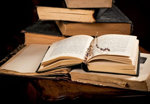 a stack of old books with bookmarks on a wooden background. A sprig of dried lavender on the page of an old book.