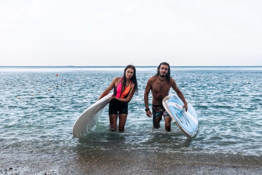 Sea woman and man on sup. Silhouette of happy young woman and man, surfing on SUP board, confident paddling through water surface. Idyllic sunset. Active lifestyle at sea or river