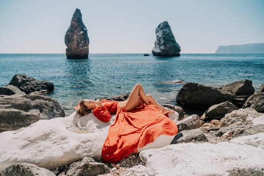 Woman travel sea. Young Happy woman in a long red dress posing on a beach near the sea on background of volcanic rocks, like in Iceland, sharing travel adventure journey
