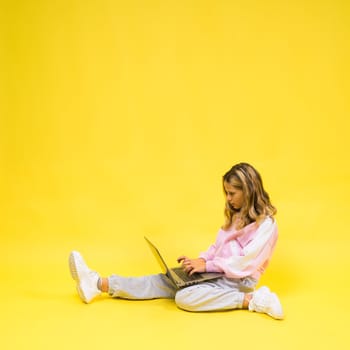 Positive kid sit with a laptop read homework wear casual style cloth isolated over yellow background
