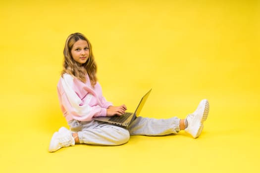 Positive kid sit with a laptop read homework wear casual style cloth isolated over yellow background