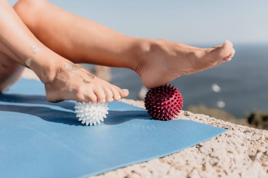 Middle aged well looking woman with black hair doing Pilates with the ring on the yoga mat near the sea on the pebble beach. Female fitness yoga concept. Healthy lifestyle, harmony and meditation.