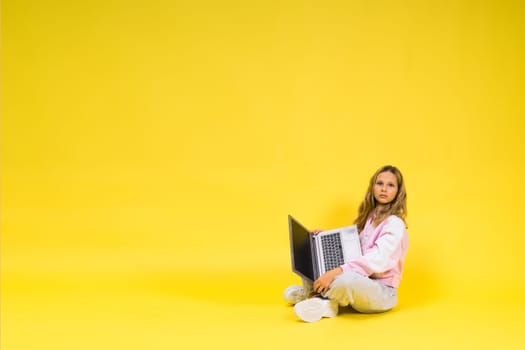 Positive kid sit with a laptop read homework wear casual style cloth isolated over yellow background