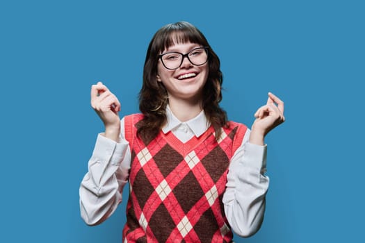 Young funny female student in glasses having fun on blue color studio background