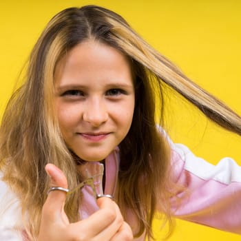 Child adorable girl hairdresser cutting long blonde hair with metallic scissors on a yellow