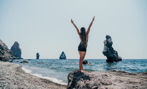 Woman travel sea. Young Happy woman in a long red dress posing on a beach near the sea on background of volcanic rocks, like in Iceland, sharing travel adventure journey