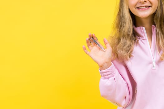 Child adorable girl hairdresser cutting long blonde hair with metallic scissors on a yellow