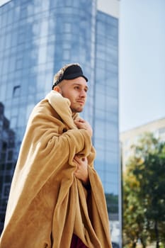 Against business building. Young man in pajama is outdoors on the street. Feels sleepy.