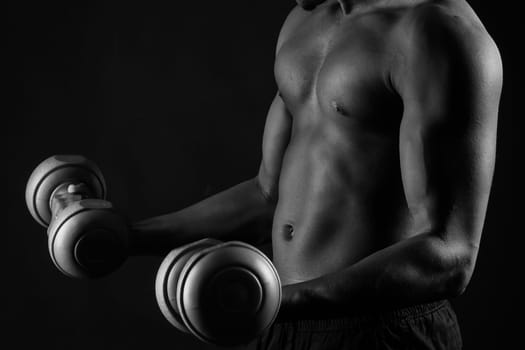 Confident young man shirtless portrait training with dumb-bell against black background.