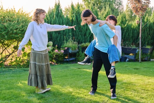 Three teenage friends having fun outdoor, sunny summer day on the lawn. Group of teenagers laughing together. Lifestyle, leisure, friendship, youth concept