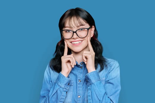 Young woman showing perfect smile with healthy teeth with rhinestone, on white studio background. Beautiful cheerful teenage girl touching cheeks with her fingers, optimistic positivity joyful concept